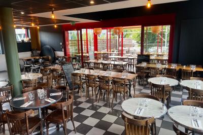 Table ronde dressée avec des verres, couverts et un centre de table en épis de blé dans un restaurant au sol carrelé.
