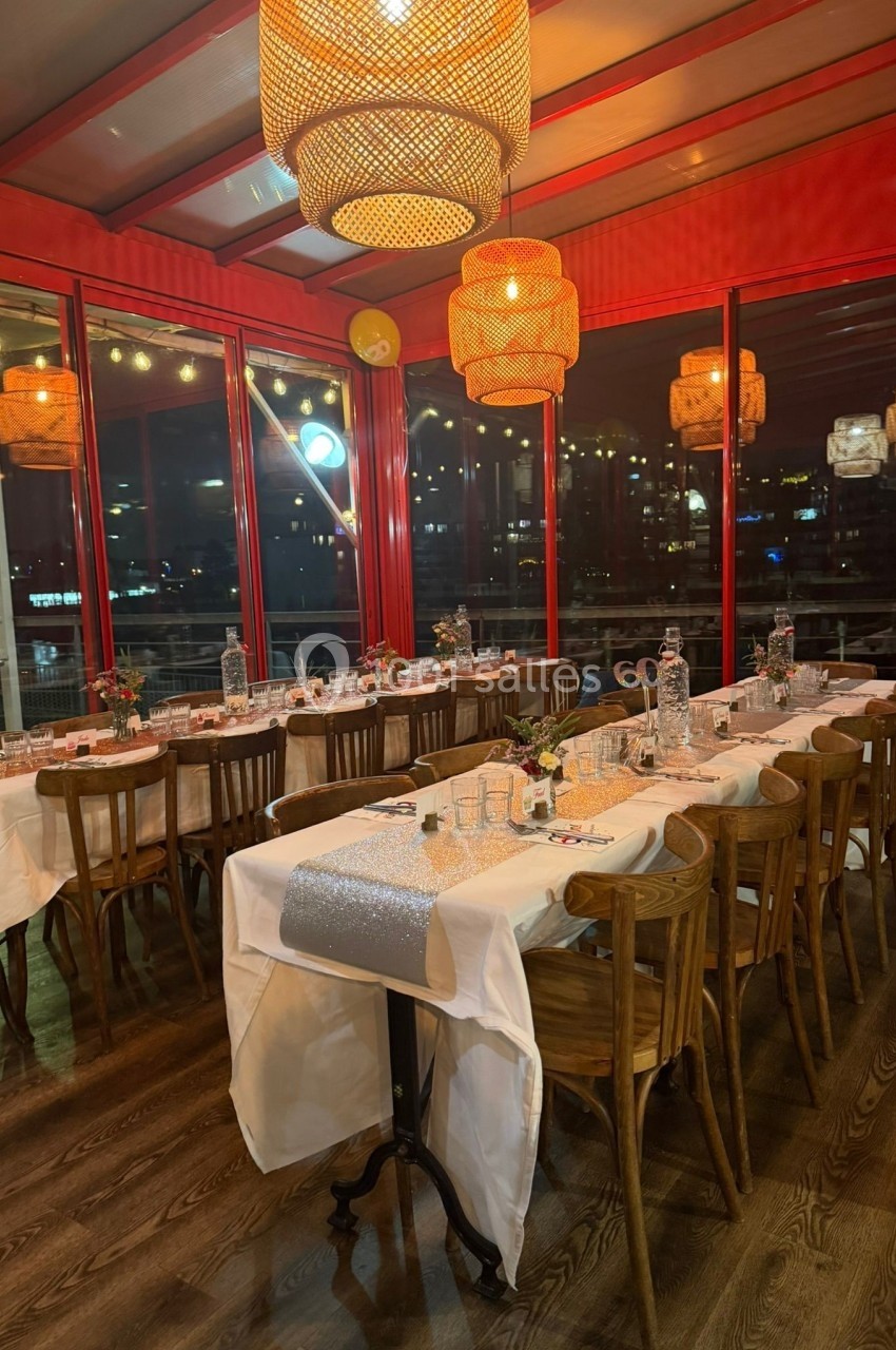 Salle de restaurant avec tables dressées, nappes blanches, chemins de table argentés et éclairage chaleureux en soirée.