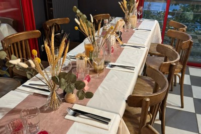 Terrasse extérieure avec tables, chaises en osier, tonneau en bois et vue sur un fleuve bordé de végétation.