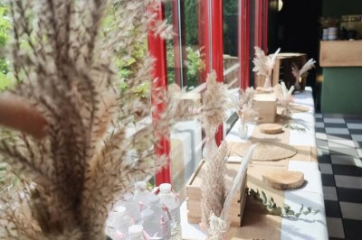 Terrasse extérieure avec tables, chaises en osier, tonneau en bois et vue sur un fleuve bordé de végétation.