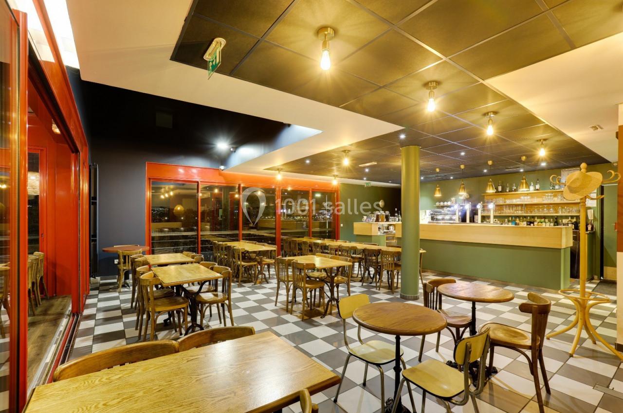 Salle de restaurant lumineuse avec tables en bois, chaises assorties et un comptoir de bar en arrière-plan.