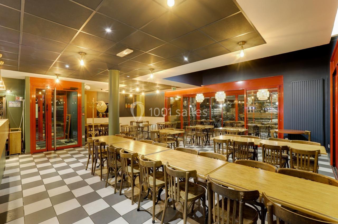Salle de restaurant lumineuse avec tables en bois, chaises assorties et sol en damier noir et blanc.