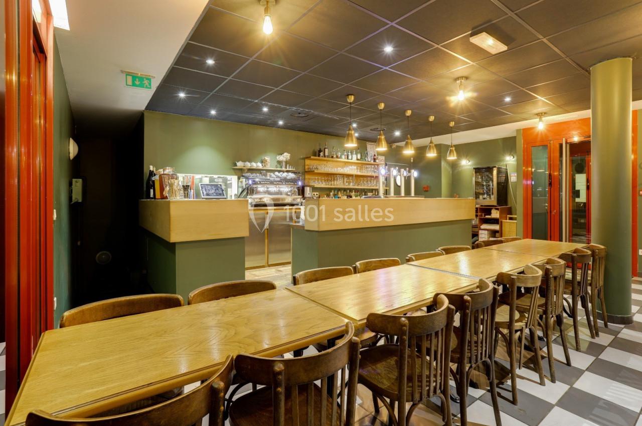 Salle de restaurant avec tables en bois alignées, chaises assorties et un comptoir éclairé en arrière-plan.