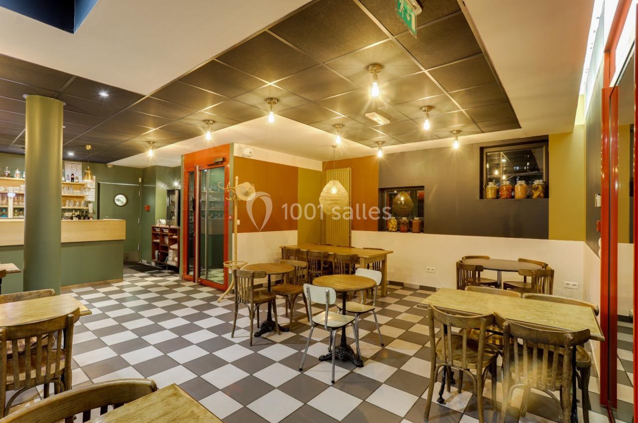 Salle de restaurant lumineuse avec tables en bois, chaises assorties et sol en carreaux noirs et blancs.