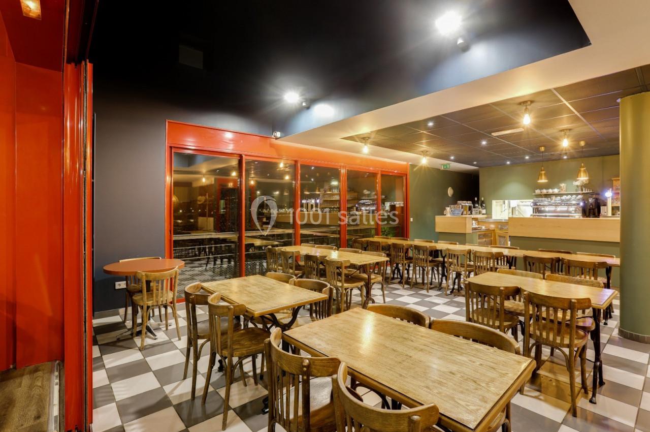 Salle de restaurant avec tables en bois, chaises assorties, éclairage chaleureux et comptoir visible en arrière-plan.