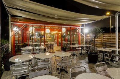 Terrasse extérieure avec tables et chaises en métal, éclairée la nuit, protégée par des toiles tendues.