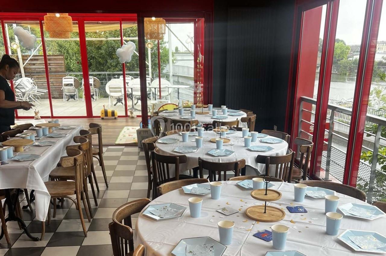 Salle de réception lumineuse avec tables dressées, vaisselle bleue et vue sur une terrasse extérieure.