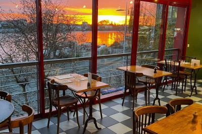 Coucher de soleil vibrant avec des nuages colorés se reflétant sur une rivière bordée d'arbres et de bâtiments.