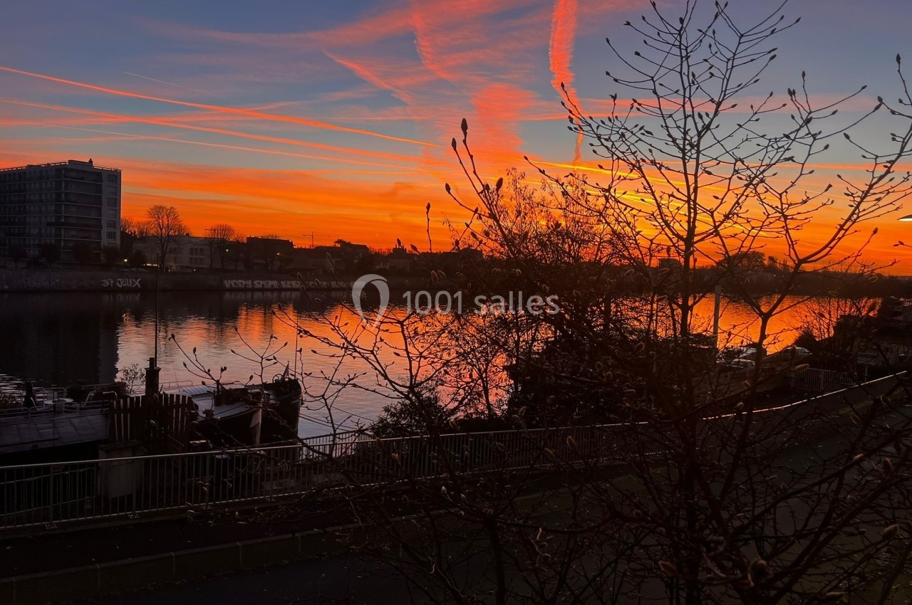 Coucher de soleil vibrant avec des nuages colorés se reflétant sur une rivière bordée d'arbres et de bâtiments.