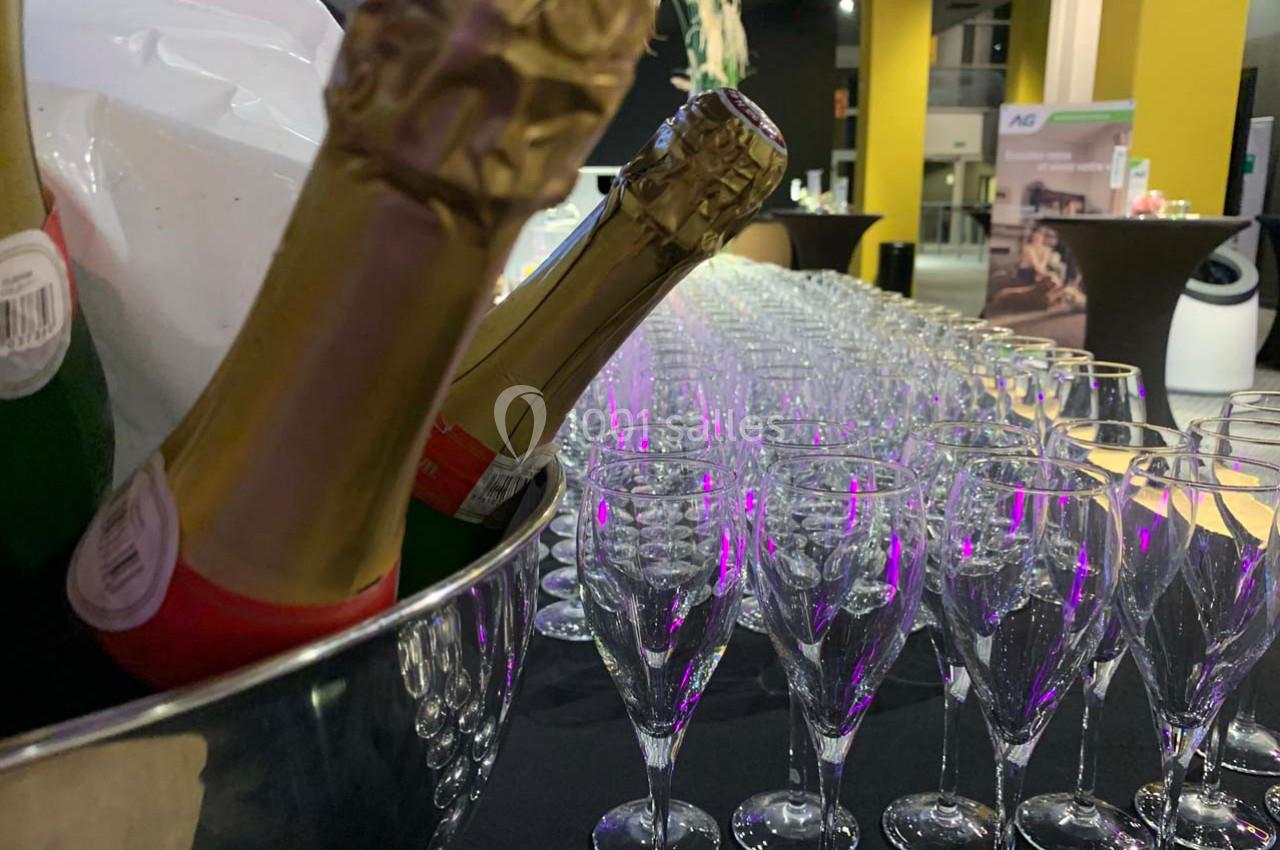 Bouteille de champagne dans un seau et rangée de flûtes vides alignées sur une table lors d'un événement.