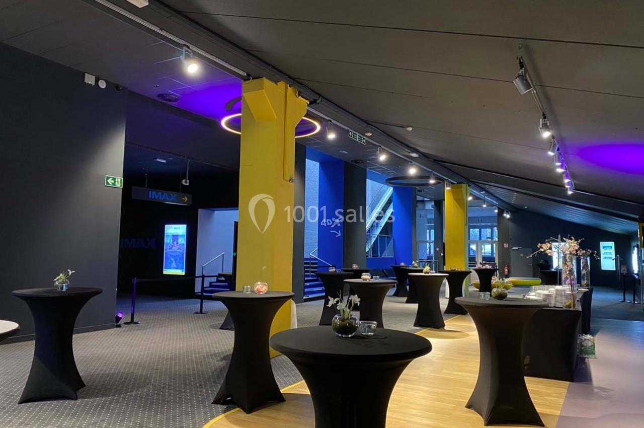 Salle moderne avec tables hautes noires, éclairage tamisé et décorations minimalistes, prête pour un événement.