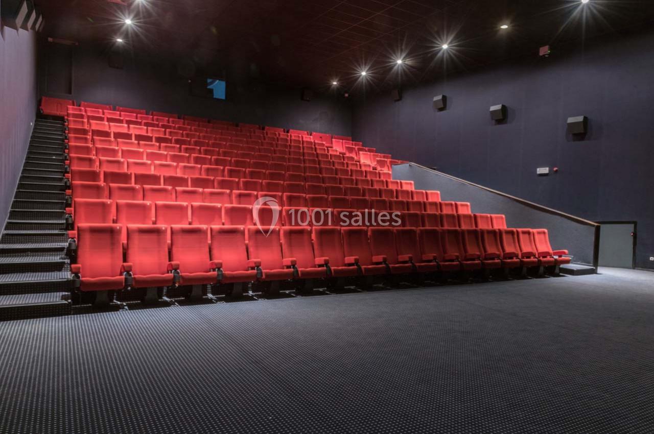 Salle de cinéma vide avec des rangées de sièges rouges et un sol recouvert de moquette sombre.