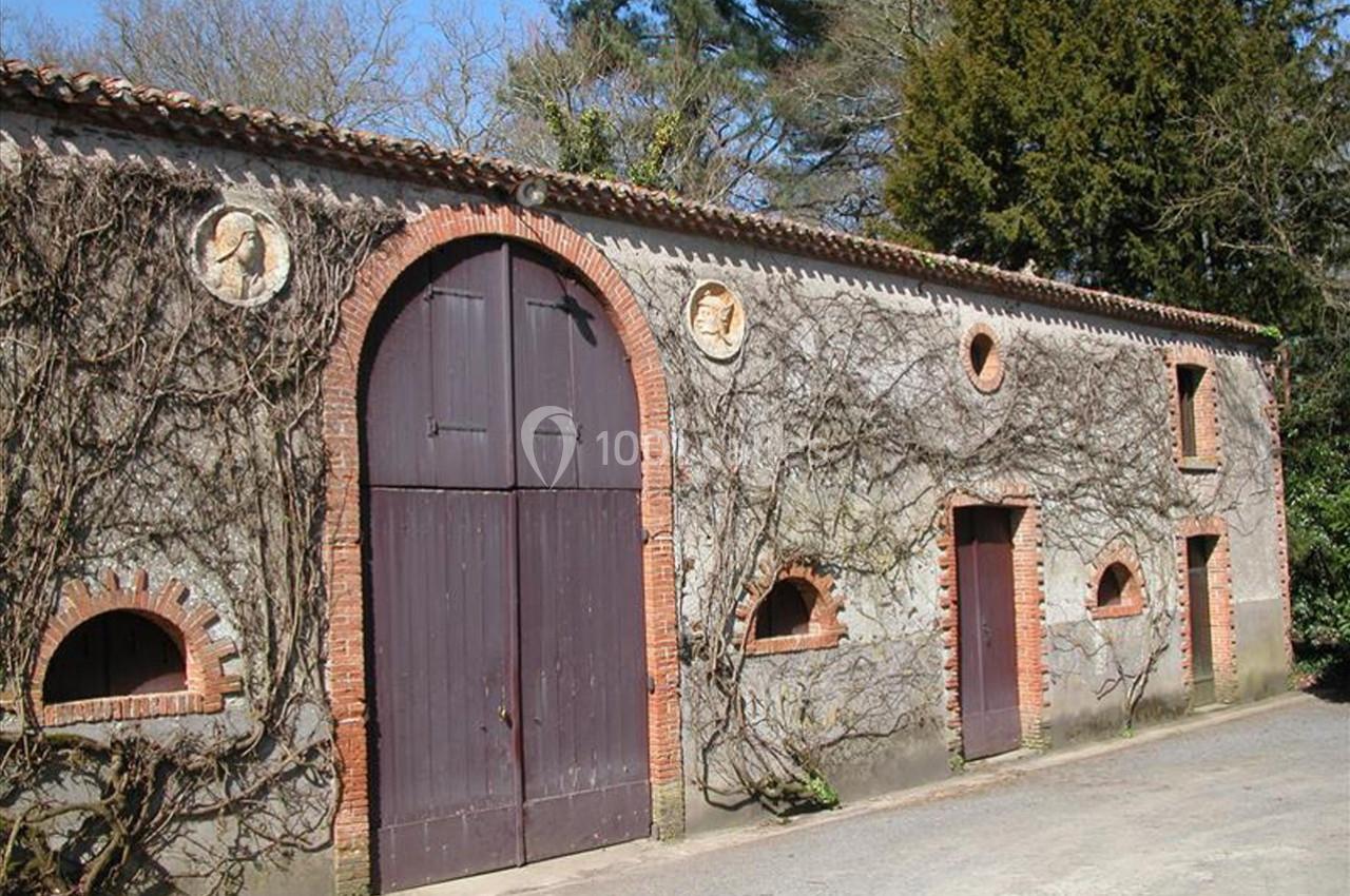 Façade en pierre d'un bâtiment ancien avec portes en bois, fenêtres arquées et vignes grimpantes.