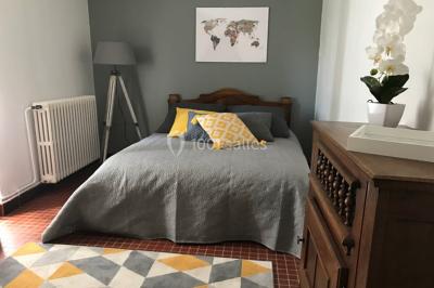 Chambre lumineuse avec lit double, fauteuils, cheminée, meubles anciens et mur décoré de motifs floraux.