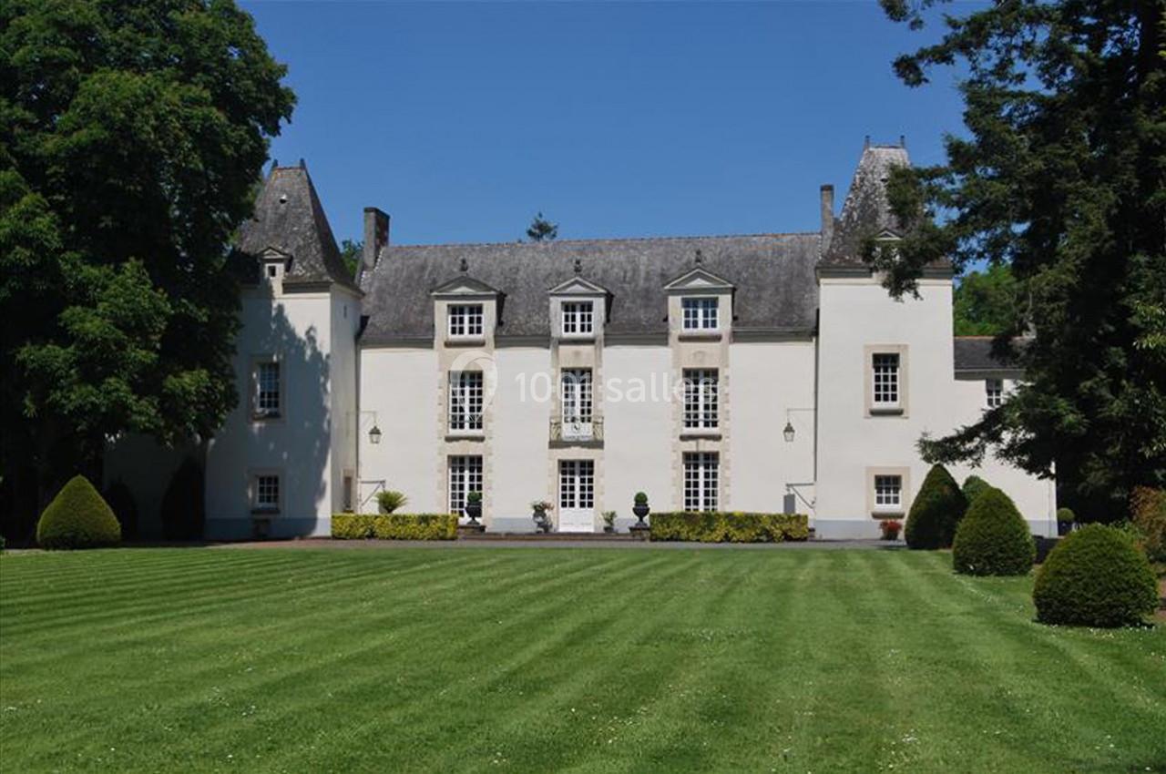Façade d'un manoir blanc entouré d'arbres, avec une pelouse bien entretenue au premier plan.