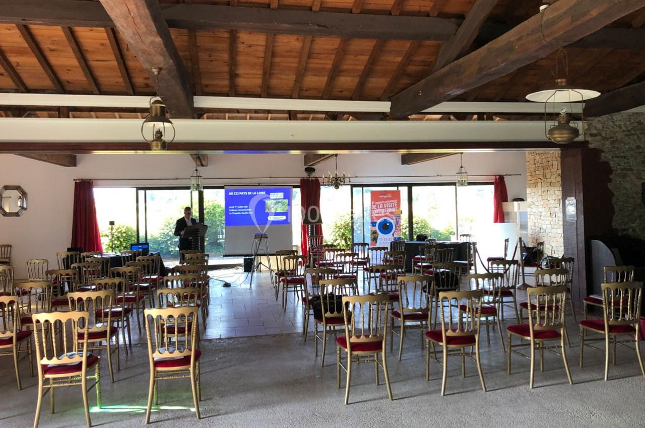 Salle de conférence avec des chaises alignées, un écran de projection allumé et des affiches promotionnelles en arrière-plan.