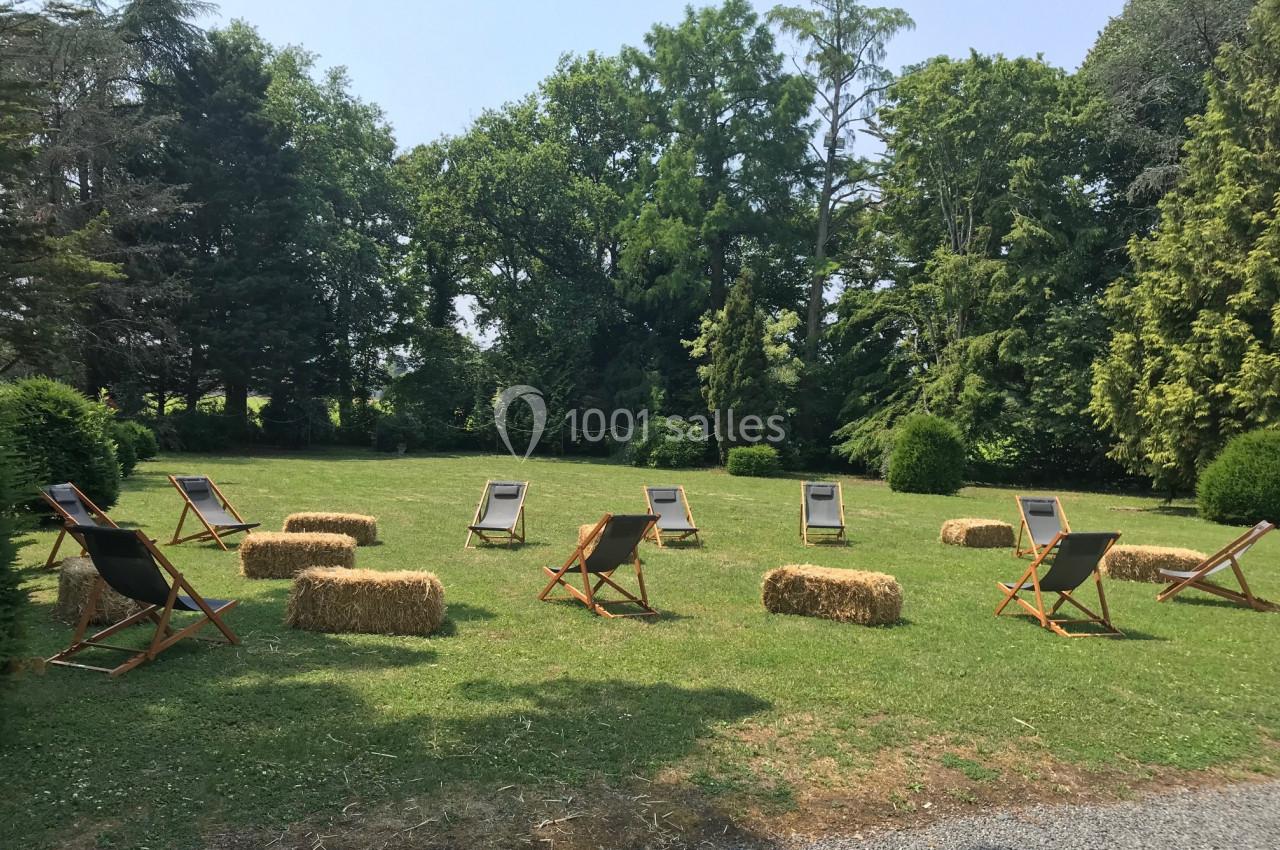 Chaises longues et bottes de paille disposées en cercle sur une pelouse entourée d'arbres.