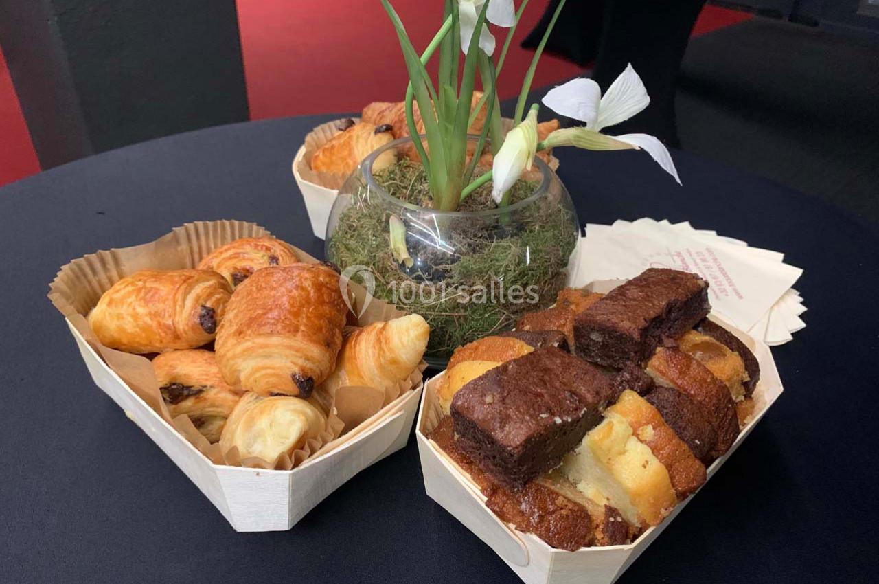 Assortiment de viennoiseries et de gâteaux disposés autour d'un vase avec des fleurs blanches sur une table noire.