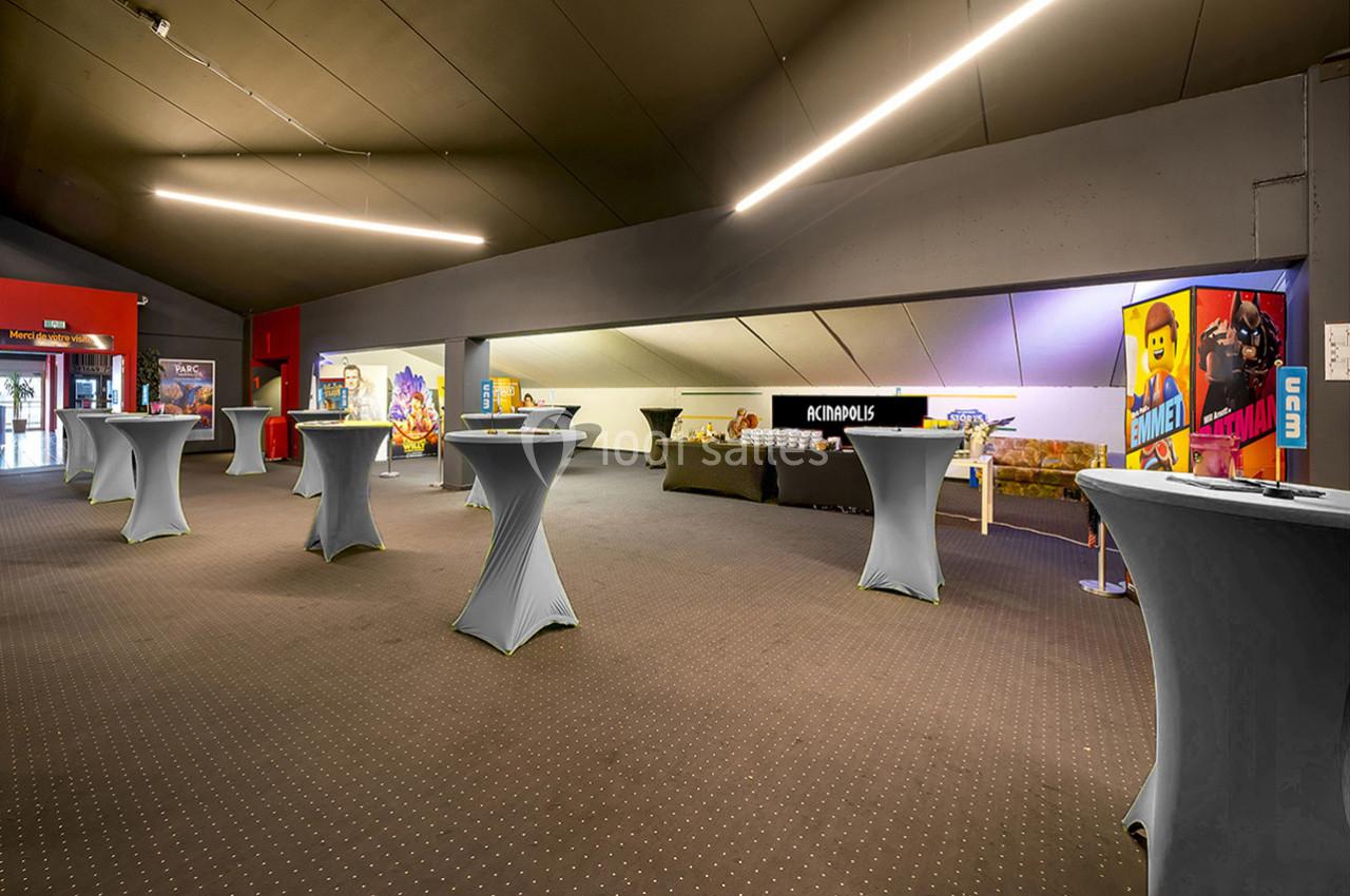 Salle avec des tables hautes recouvertes de nappes blanches, décorée avec des affiches et un stand d'accueil au fond.