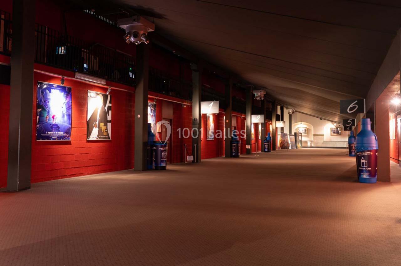 Couloir spacieux avec murs rouges, affiches lumineuses, bouteilles décoratives et éclairage tamisé.