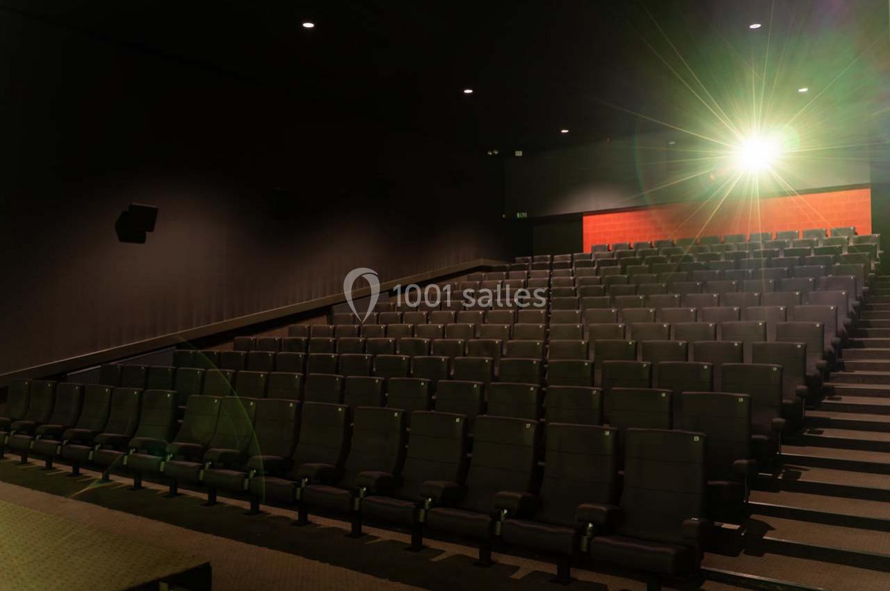 Salle de cinéma vide avec des rangées de sièges noirs et un écran illuminé en arrière-plan.