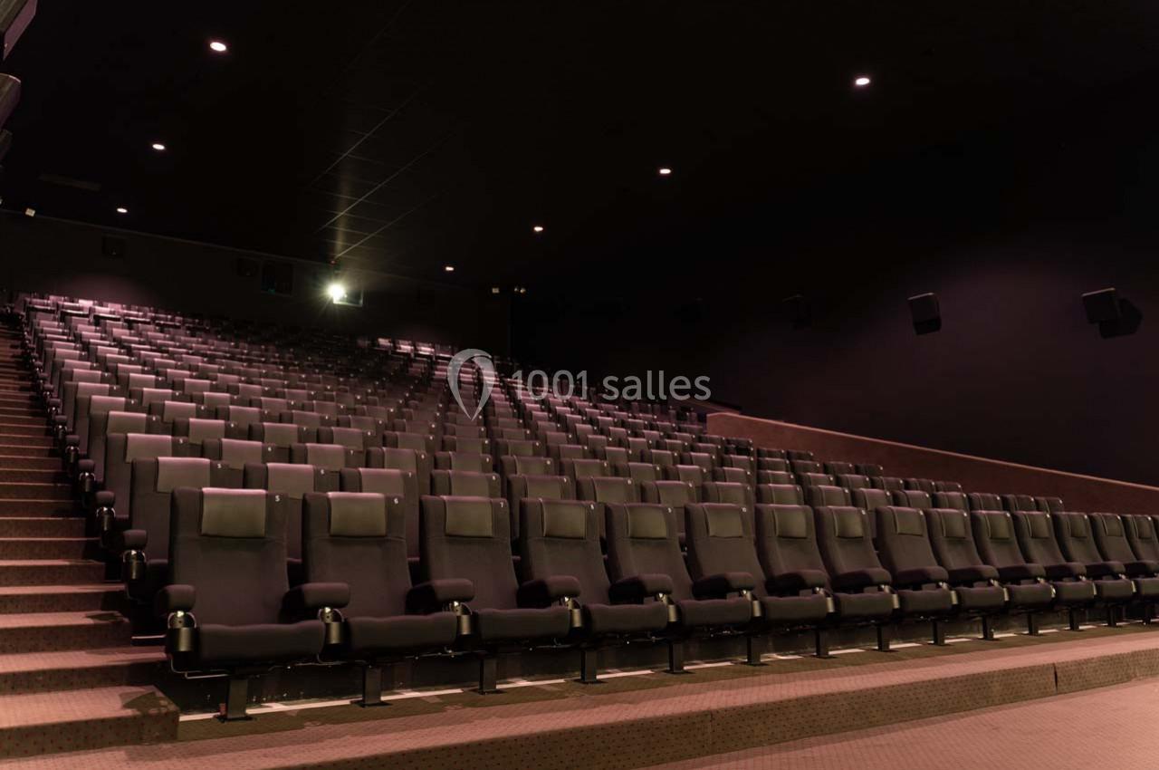 Salle de cinéma vide avec des rangées de sièges noirs alignés et un éclairage tamisé.