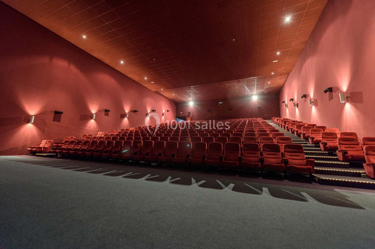 Salle de cinéma vide avec rangées de fauteuils rouges et éclairage tamisé.