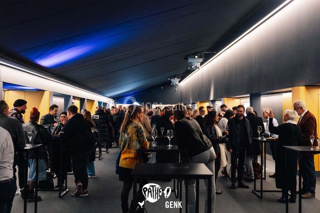 Un groupe de personnes échange dans un espace intérieur moderne avec des tables hautes et un éclairage tamisé.