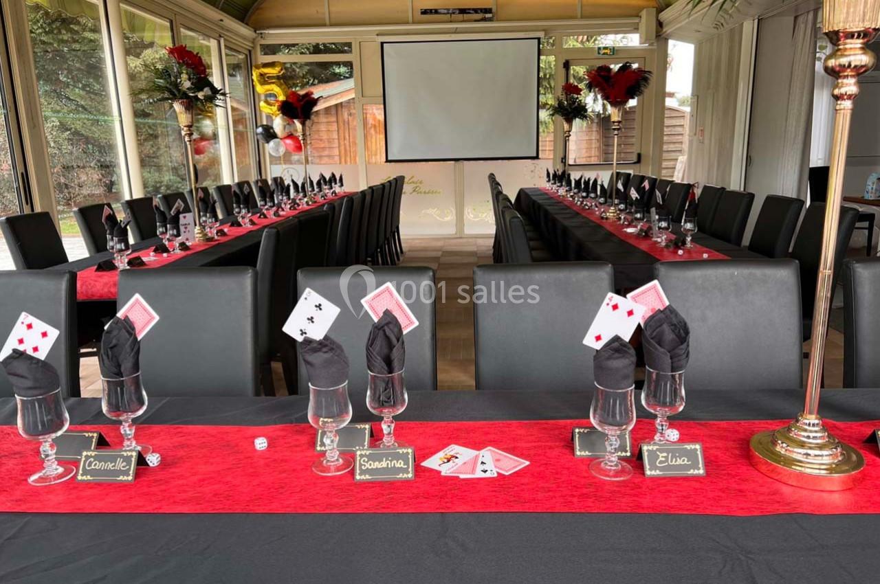 Salle décorée pour un événement avec une longue table dressée, nappes rouges, cartes à jouer et porte-noms personnalisés.