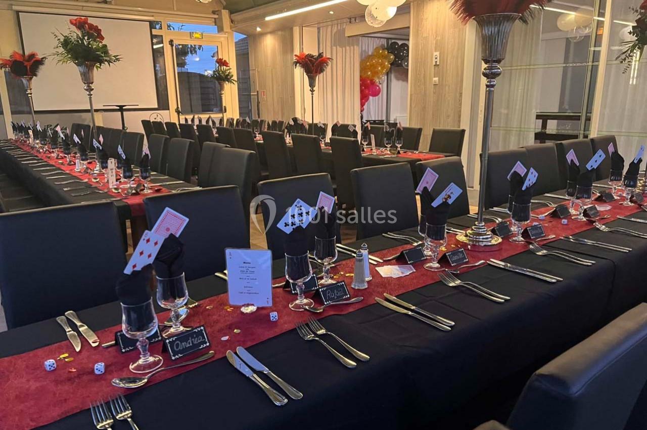 Salle de réception décorée sur le thème du casino avec tables dressées, cartes à jouer et dés en centre de table.
