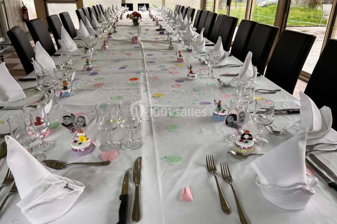 Grande table dressée pour un repas festif, avec nappes blanches, serviettes pliées, couverts et décorations colorées.