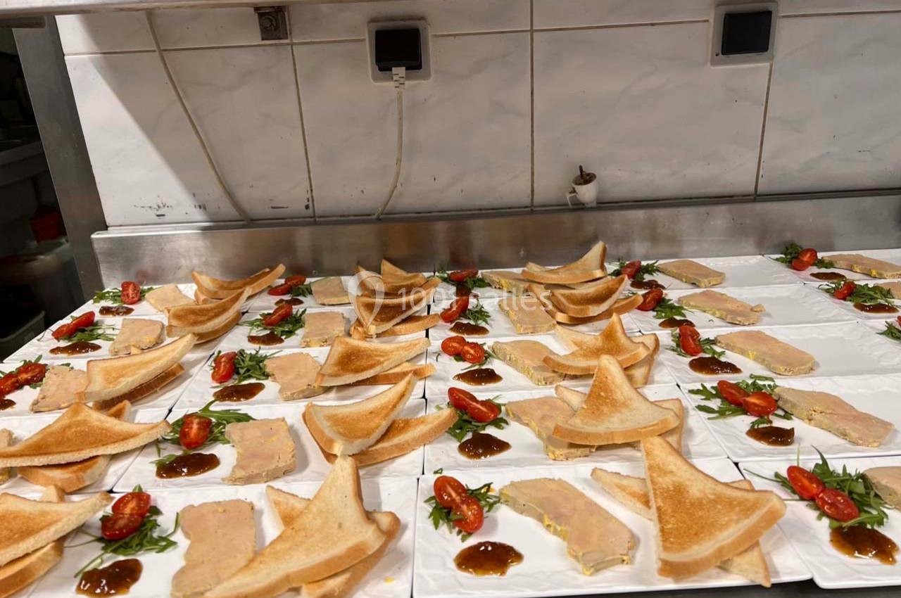 Assiettes dressées avec des tranches de foie gras, toasts triangulaires, tomates cerises et sauce sur un plan de travail.