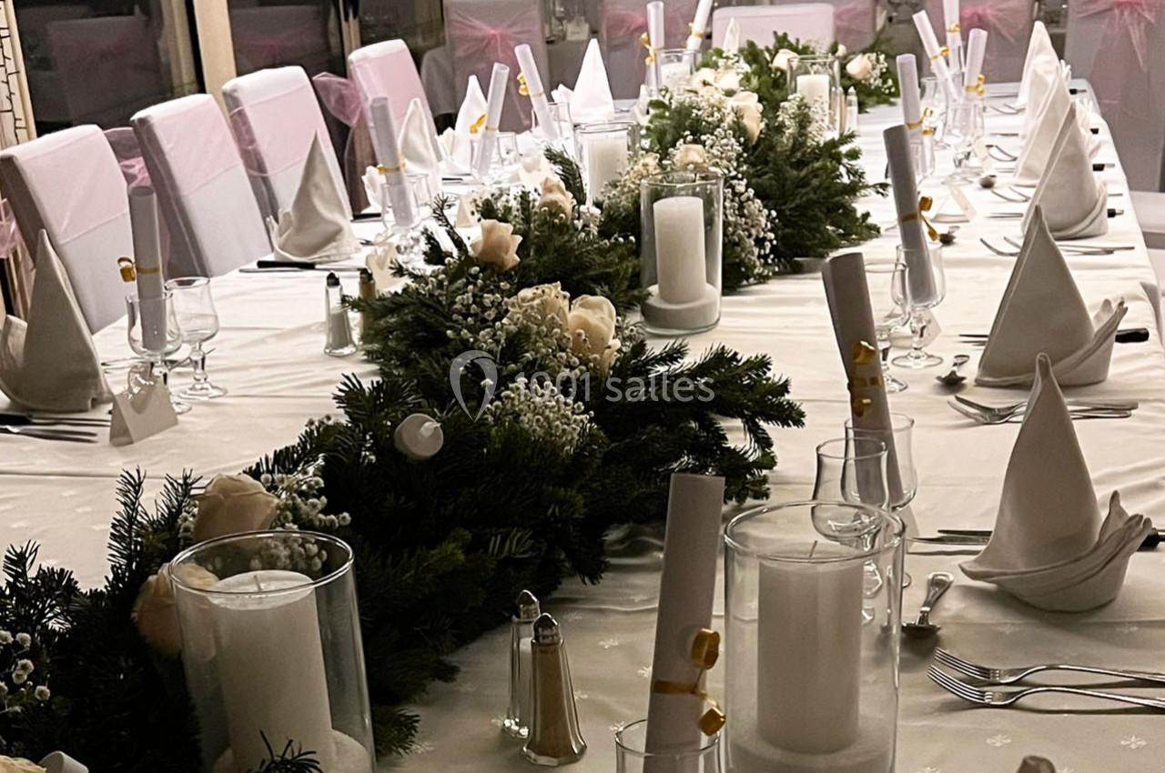 Table élégamment dressée avec nappes blanches, serviettes pliées, bougies et décorations florales.