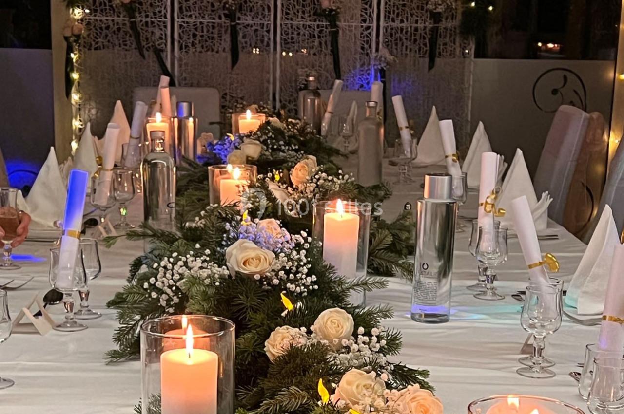 Table décorée pour un dîner festif avec bougies allumées, fleurs blanches et serviettes pliées sur une nappe blanche.