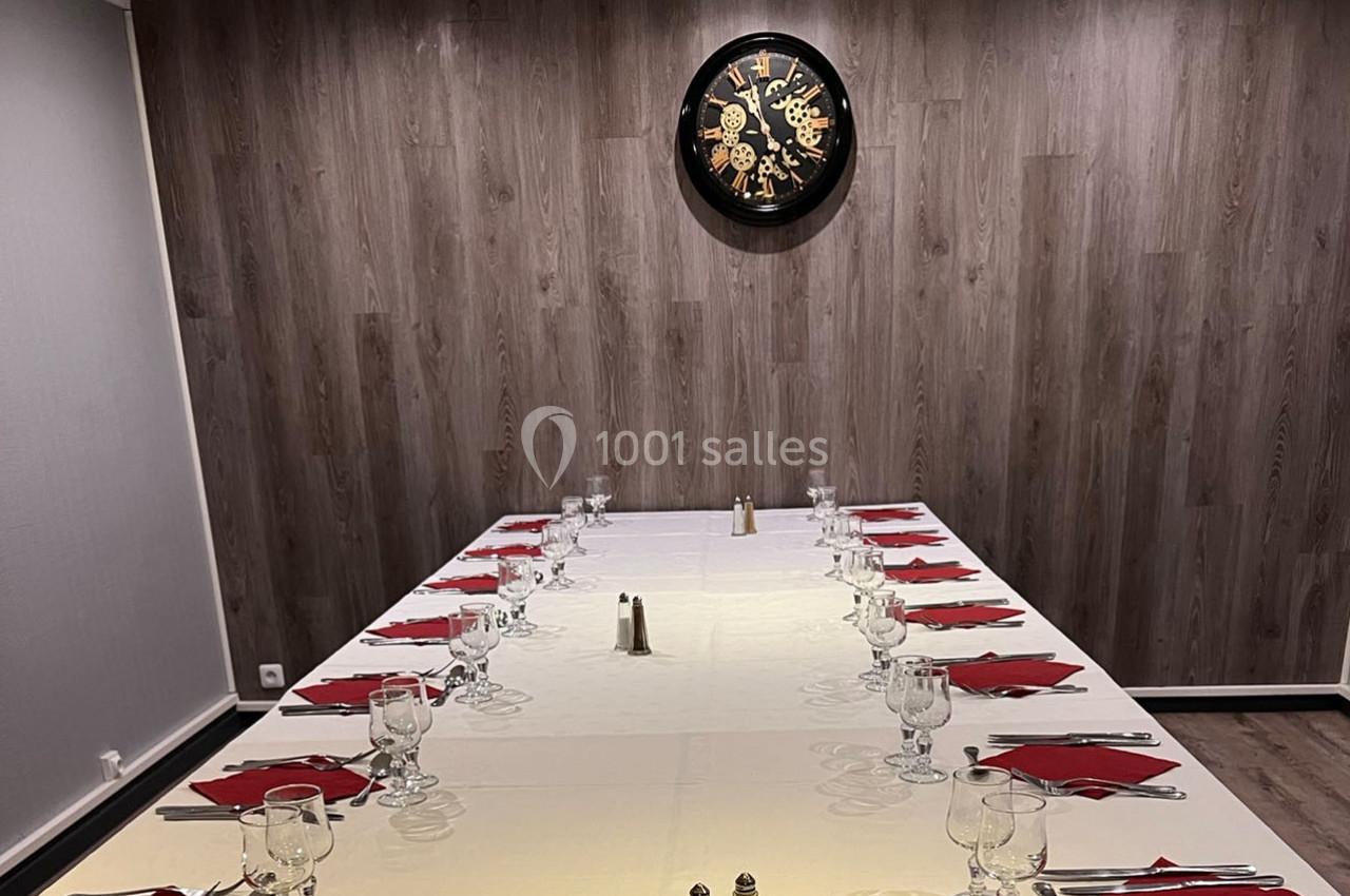 Table dressée pour un repas, avec nappes blanches, serviettes rouges, verres et couverts, dans une salle au mur boisé.