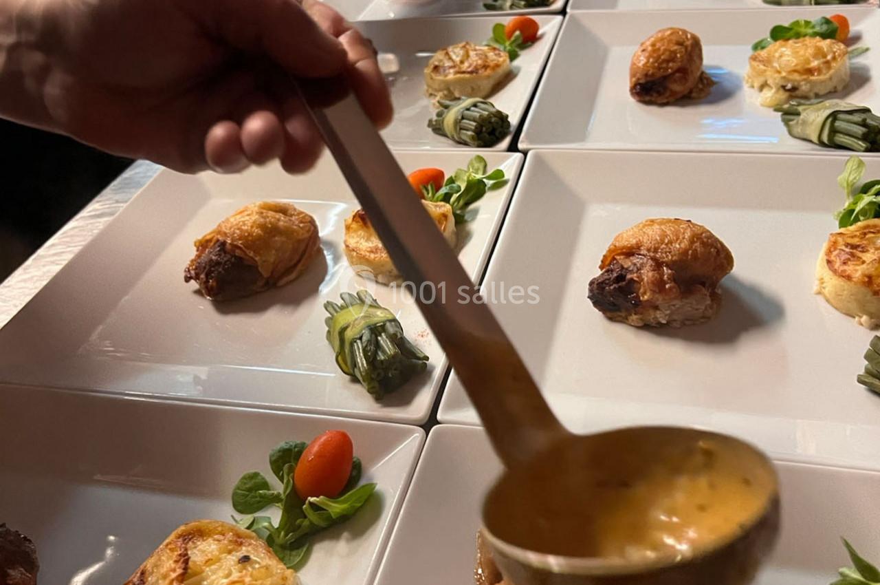 Des assiettes dressées avec des plats raffinés, une main verse une sauce à l'aide d'une louche.