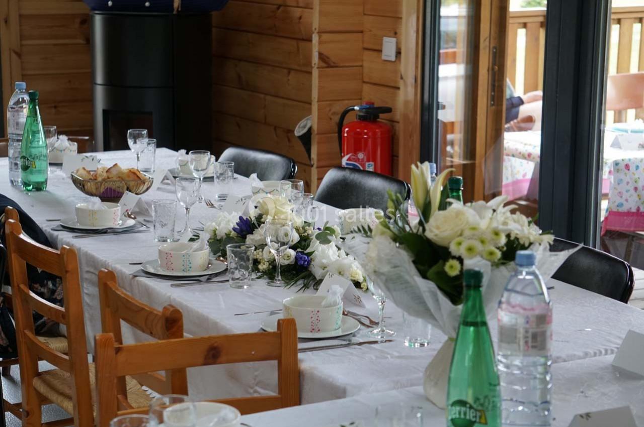 Table dressée avec nappes blanches, vaisselle, bouquets de fleurs et bouteilles d'eau dans une salle en bois.