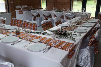 Salle décorée pour un repas festif, avec tables dressées, nappes blanches et touches de tissu coloré.