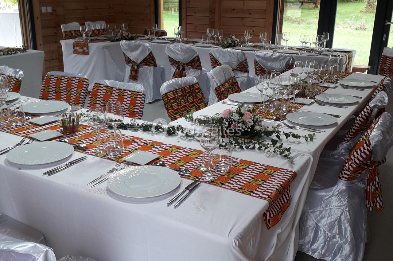 Salle décorée pour un repas festif, avec tables dressées, nappes blanches et touches de tissu coloré.
