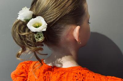Femme de dos avec des cheveux blonds coiffés en tresse et chignon, portant un pull beige près d'une fenêtre.