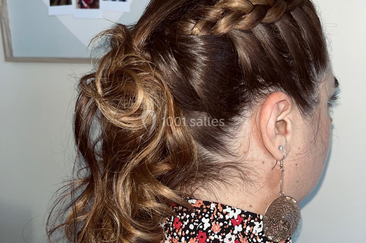 Femme de dos avec une coiffure tressée et attachée, portant une blouse fleurie et des boucles d'oreilles pendantes.