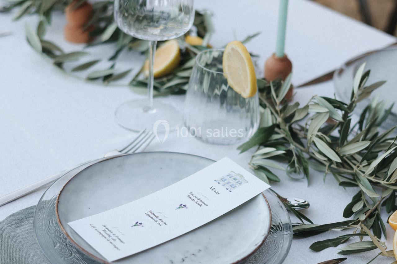 Table dressée avec assiette, menu, verres, bougies et décoration végétale incluant des branches d'olivier et des tranches de…