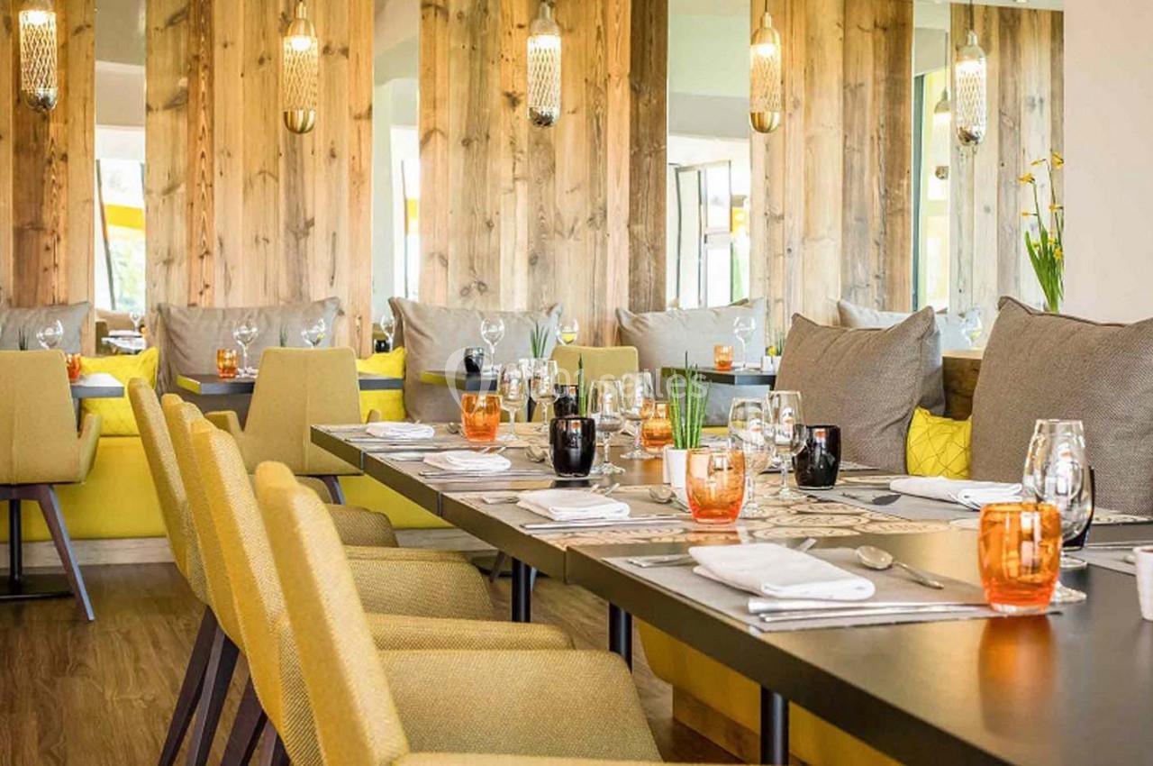 Salle de restaurant lumineuse avec tables dressées, chaises jaunes, murs en bois et miroirs décoratifs.