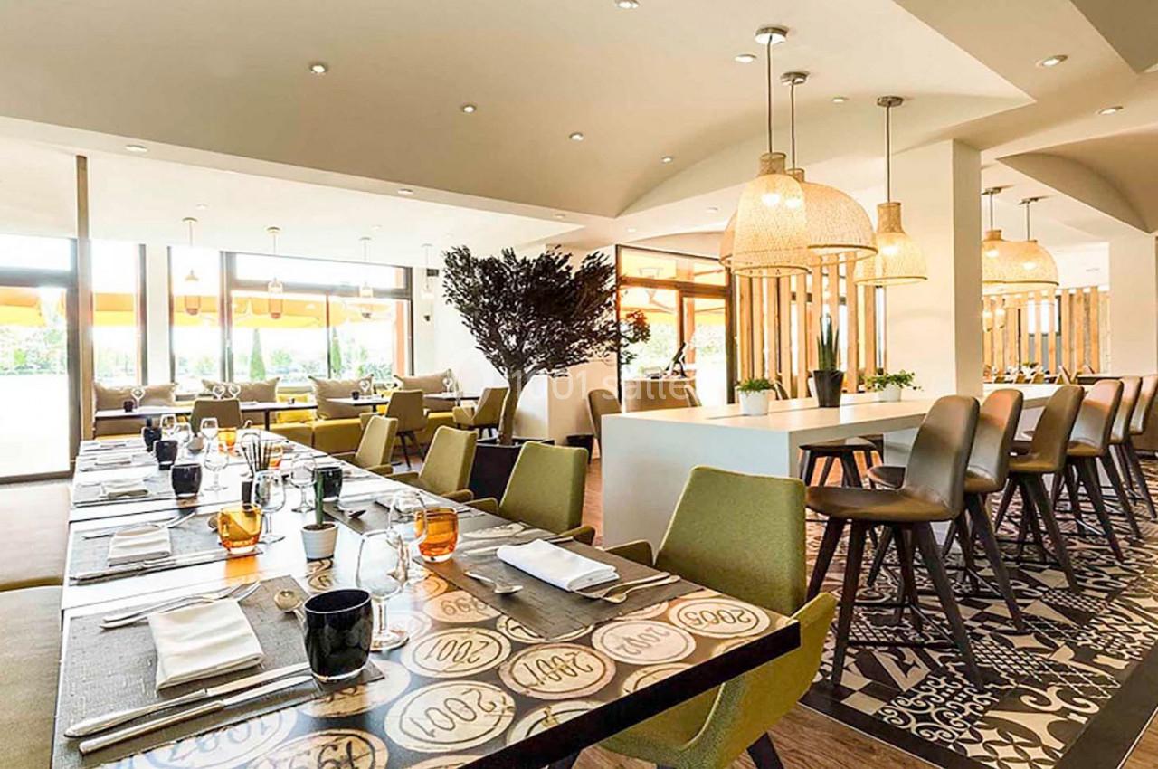 Salle de restaurant lumineuse avec tables dressées, chaises modernes et suspensions en osier.
