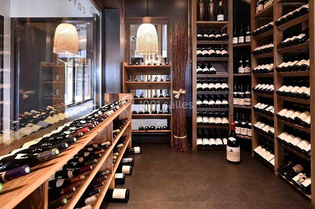 Cave à vin avec étagères en bois remplies de bouteilles, éclairée par des suspensions en osier.