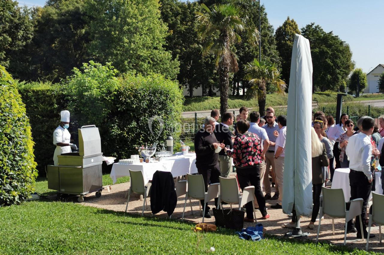 Groupe de personnes rassemblées en extérieur autour de tables dressées, avec un chef près d'un barbecue.