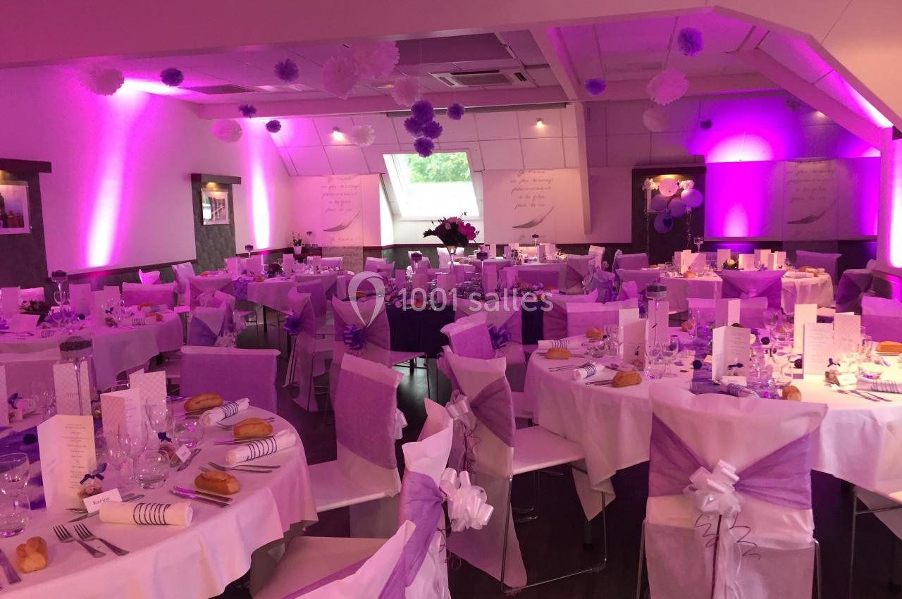 Salle de réception décorée en violet et blanc avec tables dressées pour un événement festif.