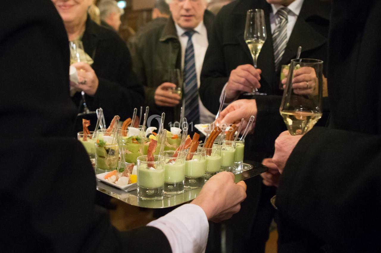 Personnes debout dégustant des verrines et des amuse-bouches lors d'un événement avec des verres de vin à la main.