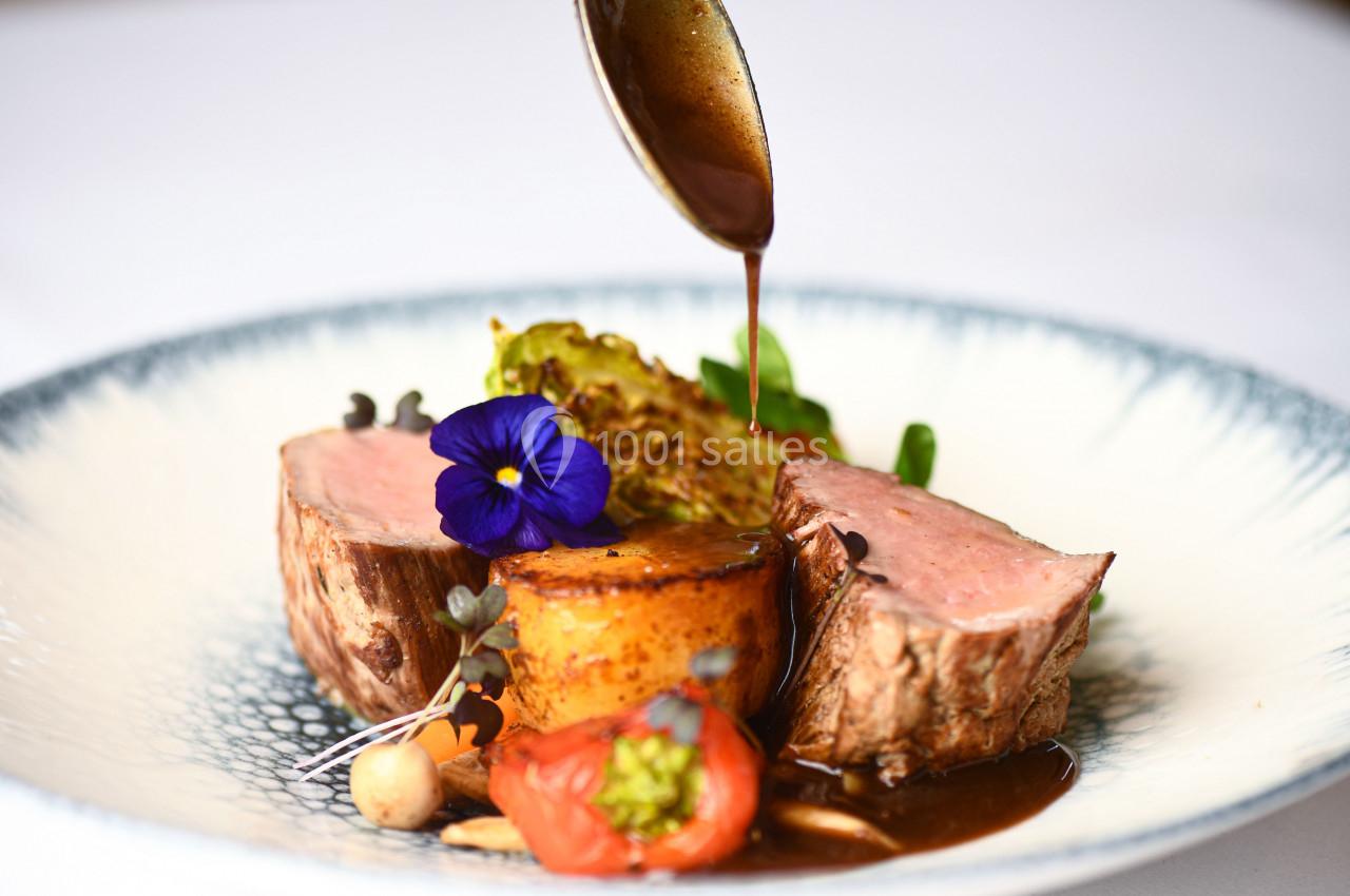 Assiette gastronomique avec viande rosée, légumes, fleur comestible et sauce versée délicatement.