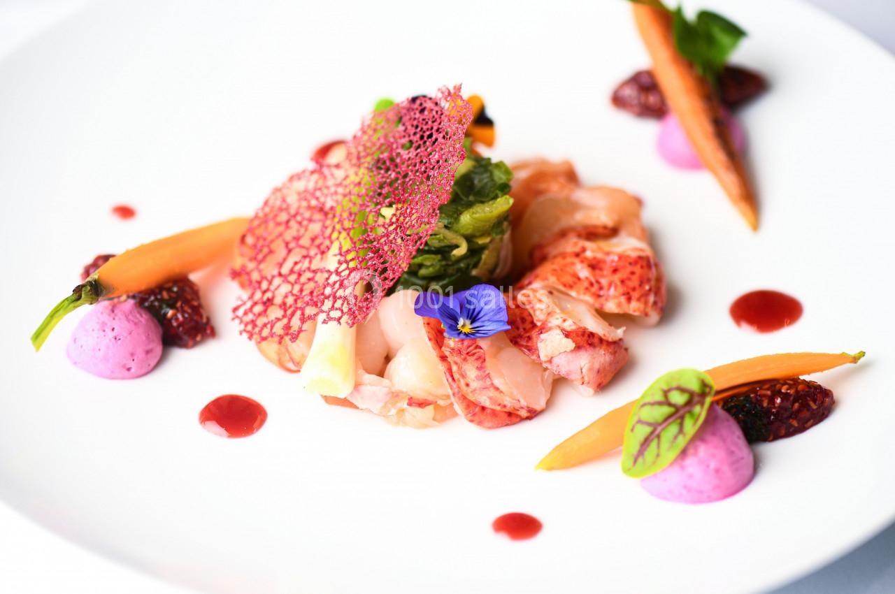 Assiette gastronomique avec homard, légumes colorés, mousse rose, sauce rouge et décoration florale.
